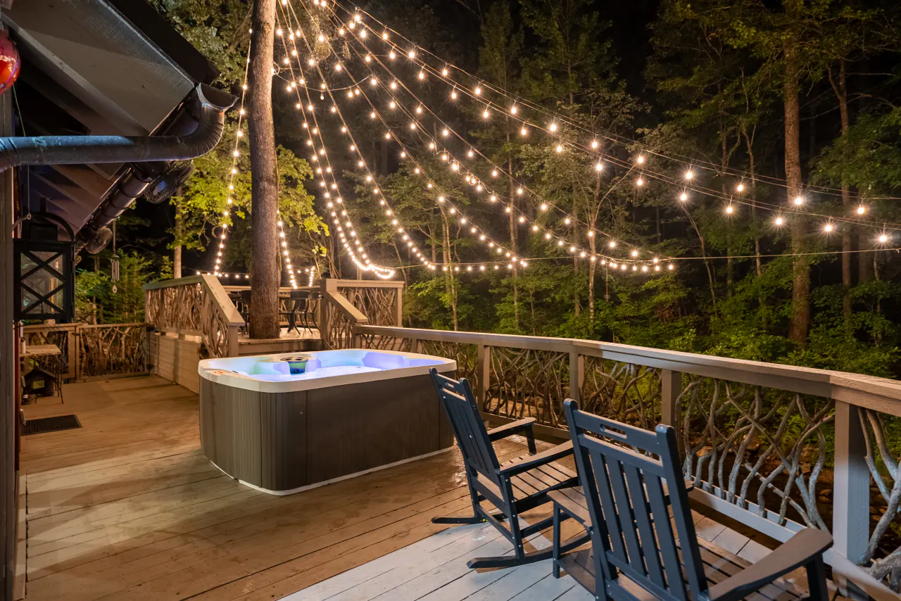 The Riverfront Hideaway hot tub glowing under string lights on the riverfront deck at night